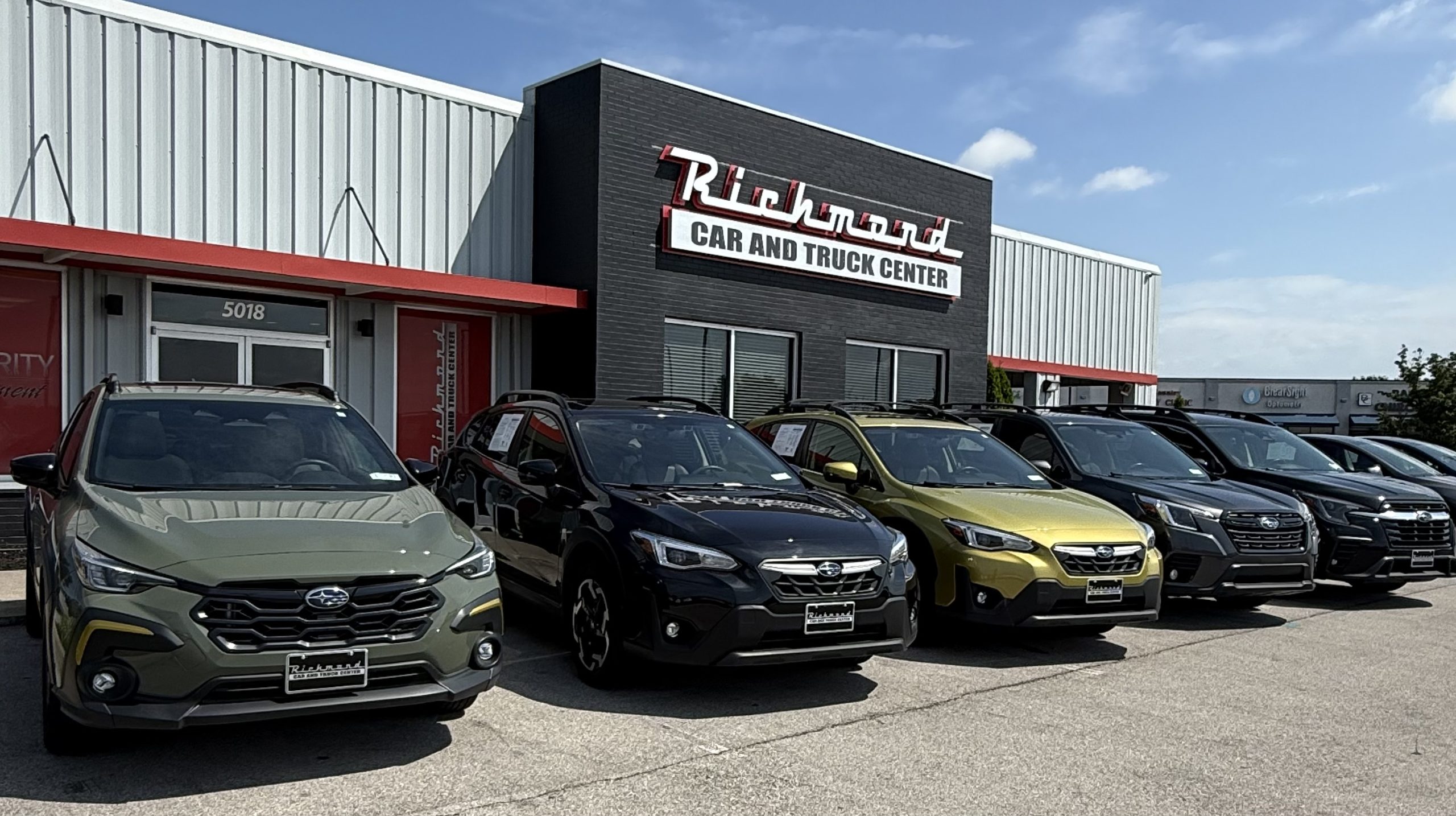 Green Subaru Crosstrek, Black Subaru Crosstrek, Yellow Subaru Crosstrek, Gray Subaru Forester, and Black Subaru Ascent lined up in front of Richmond Car and Truck Center, a used car dealership in Richmond, KY