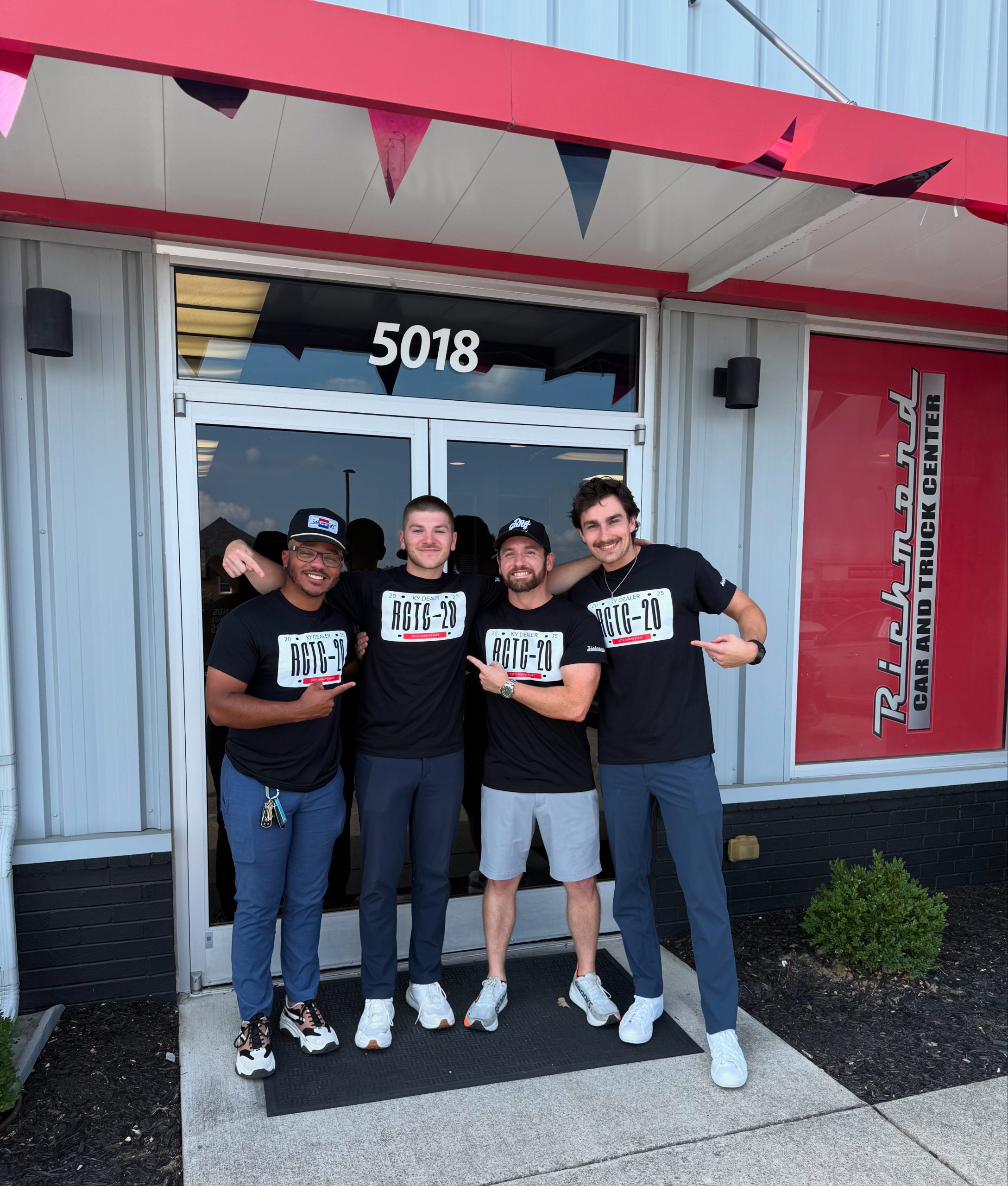 Four males, Devin, Bradyn, Wesley, and Jason model the Richmond Car and Truck Center 20th anniversary shirts featuring a dealer plate design